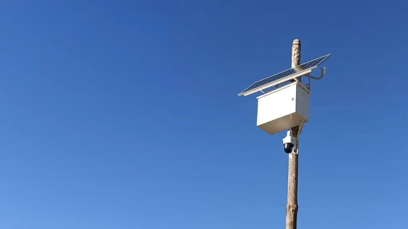 Solar-powered CCTV camera on a wooden pole against a blue sky