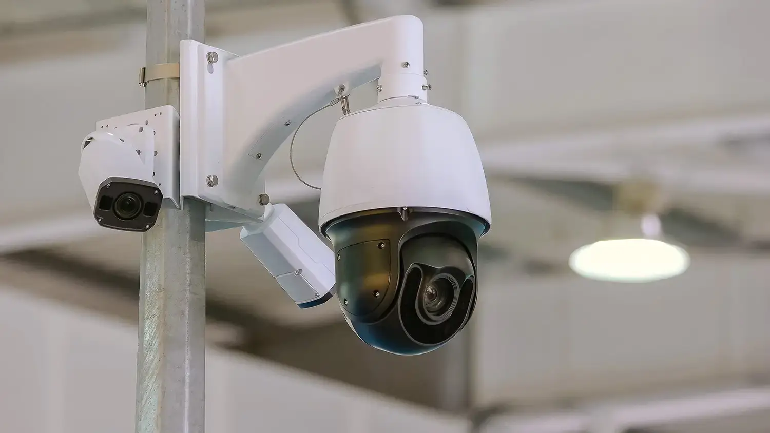 PTZ speed dome and fixed bullet CCTV camera on a pole bracket inside a warehouse