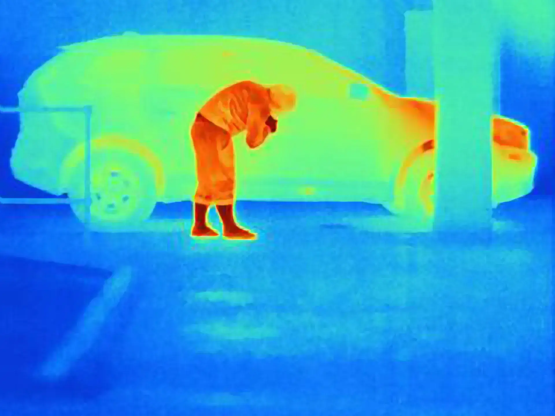 Thermal camera image of a person breaking into a parked car at night