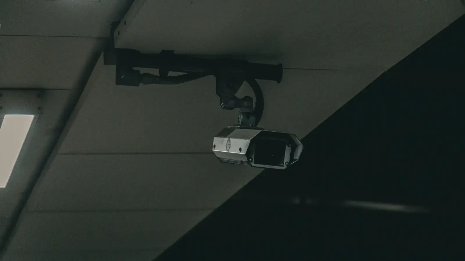 CCTV camera on a bracket mounted under a dark concrete ceiling