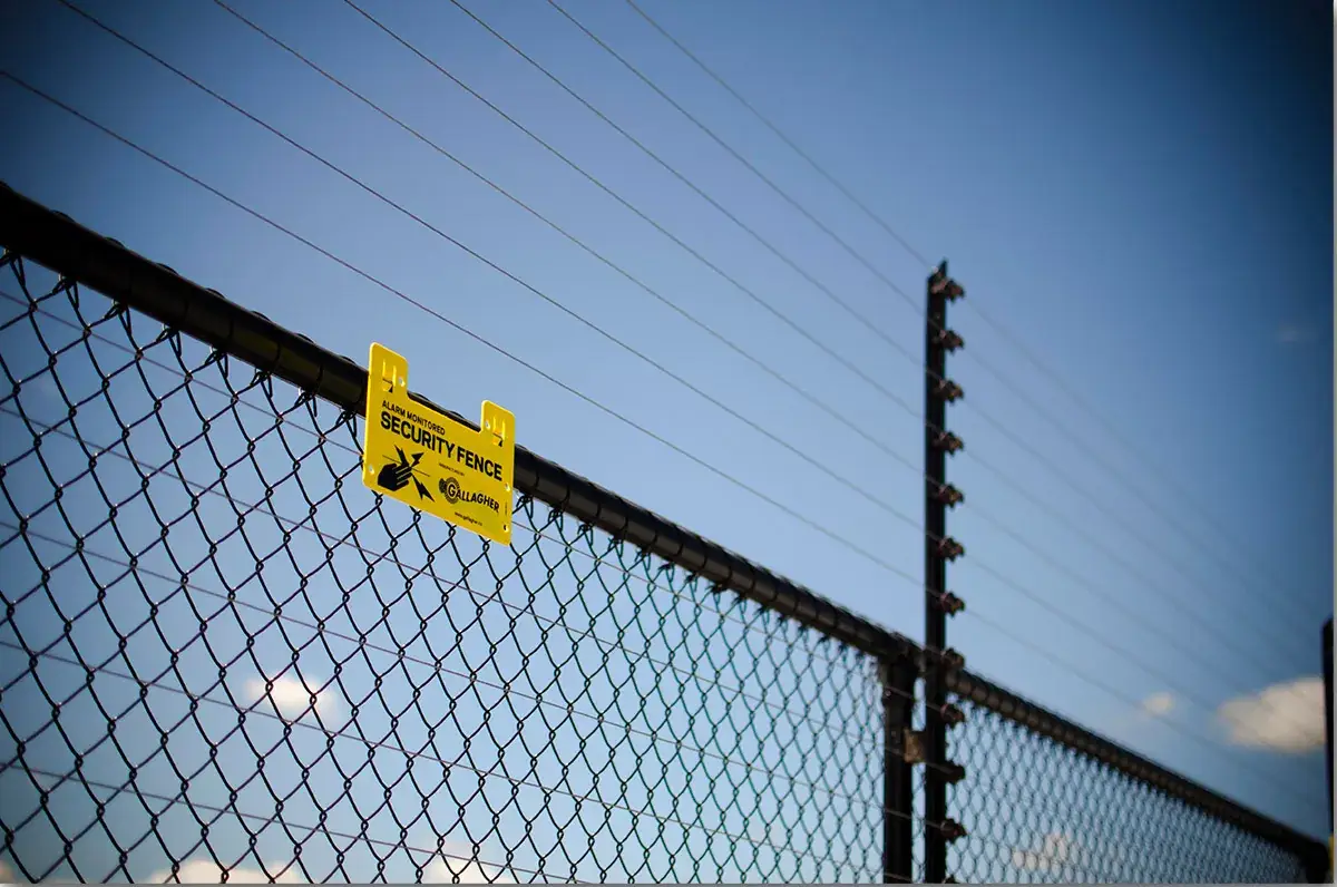 Electric security fence with a yellow warning sign on a chain-link perimeter