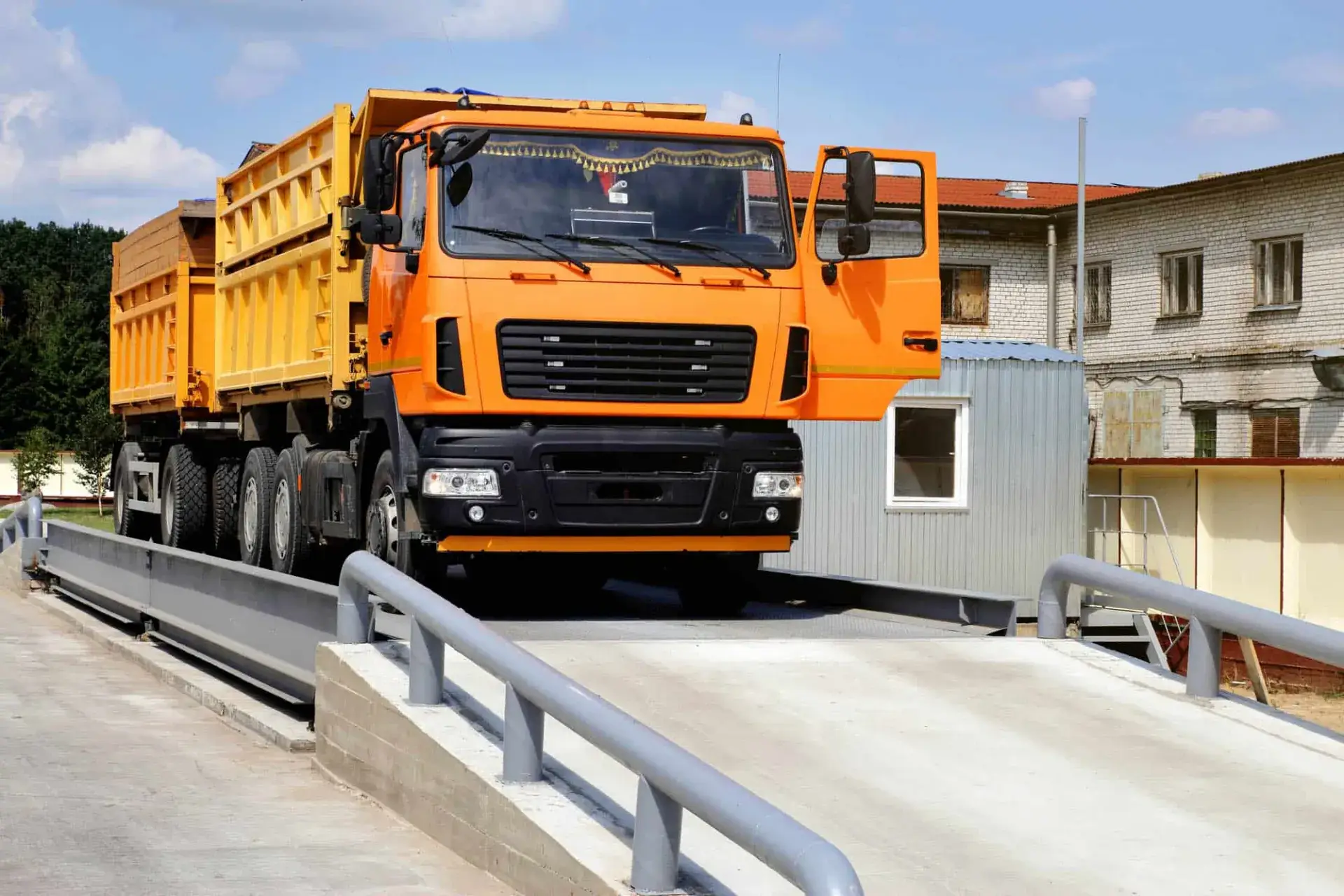 Loaded orange tipper truck driving onto a weighbridge