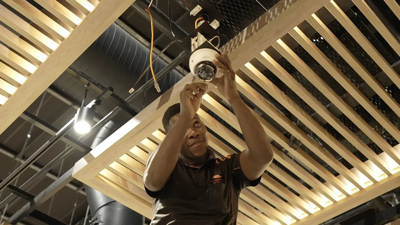 CCTV Security Surveillance technician fitting a Dahua dome camera into a slatted store ceiling