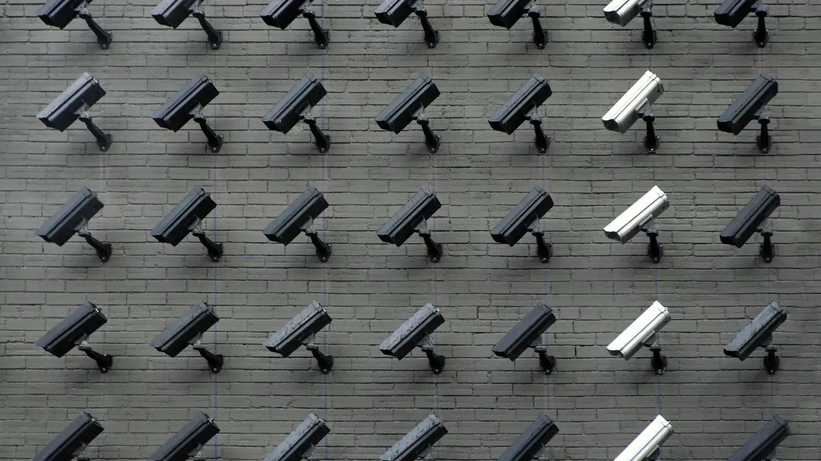 Rows of CCTV security cameras mounted on a grey brick wall