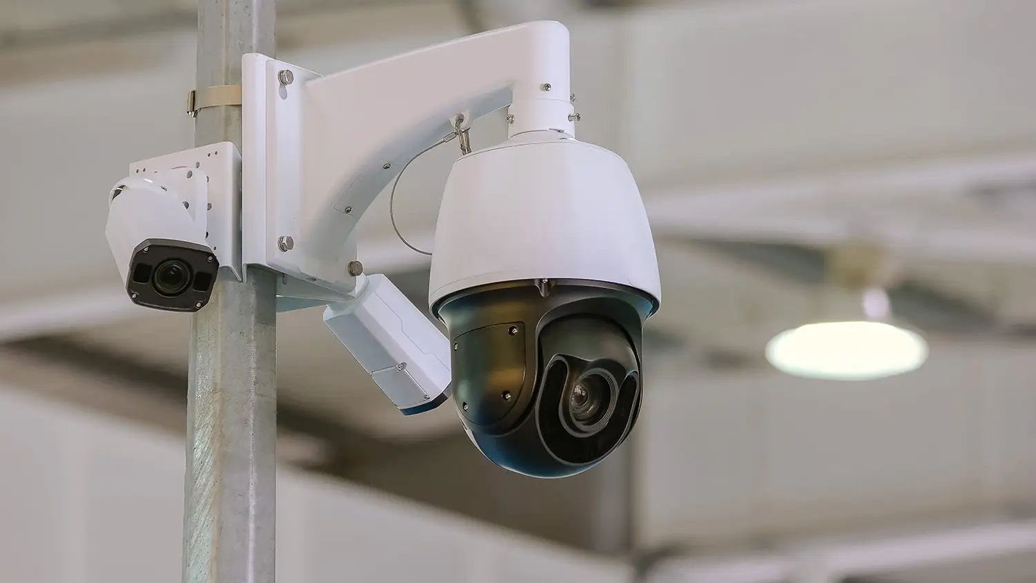 PTZ speed dome and fixed bullet CCTV camera on a pole bracket inside a warehouse, combining wide-area tracking with a fixed view