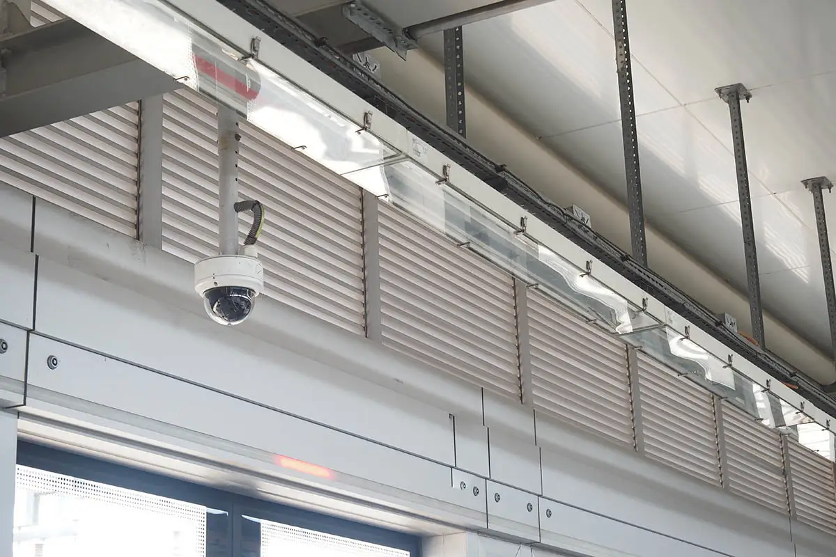 Indoor dome CCTV camera on a ceiling pendant mount above a warehouse entrance, covering staff and goods moving through the doorway